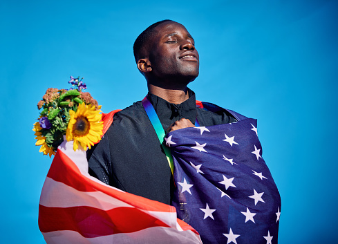 Proud athlete draped in the flag of the USA. Outdoor celebration portrait with blue sky background. Sports victory and happiness concept.