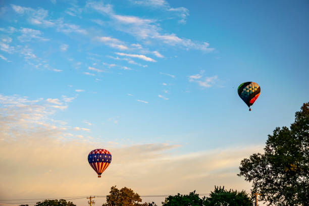 As dusk settles in, two hot air balloons, one adorned with the stars and stripes, grace the evening sky with a display of patriotic pride and peaceful flight.