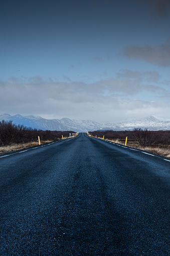 Empty road across Icelandic highlands with snowy mountains on the horizon