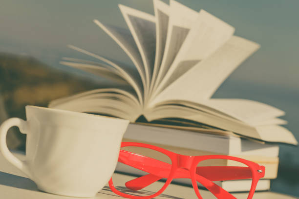 Reading on holidays. Coffee cup and books on table outdoors against blue sea water background. Book pages fluttering in the wind.