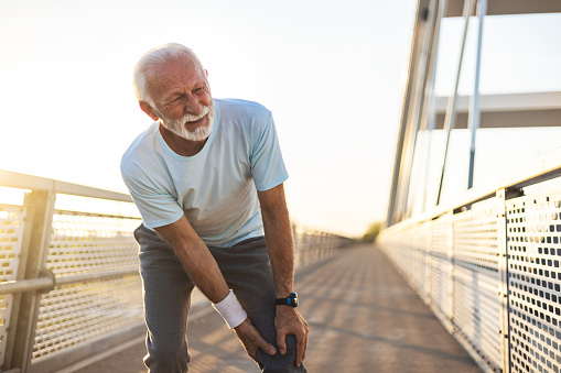 Shot of a mature man experiencing knee pain. mature man experiencing knee pain while exercising outdoors.