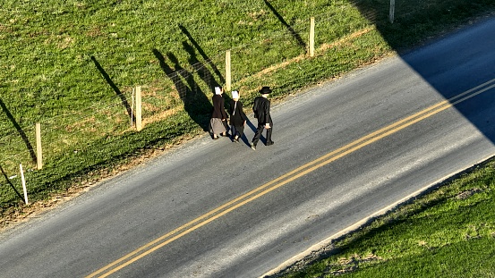 Ronks, Pennsylvania November 14, 2023 - Cast by the low sun, the elongated shadows of three individuals, Amish walking down a rural road paint a picture of camaraderie and community.