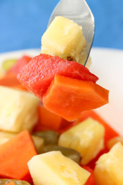 istock Full frame image of white bowl containing tropical fruit salad forkful of fruit, ingredients for self made fruit salad, chopped papaya, pineapple, watermelon, seedless white grapes and satsuma segments, blue background, focus on foreground 2149986569
