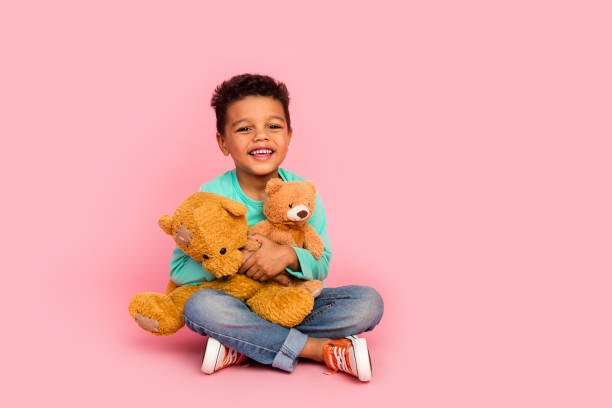 Full length photo of adorable little boy sit floor hold two teddy bears dressed stylish cyan garment isolated on pink color background Full length photo of adorable little boy sit floor hold two teddy bears dressed stylish cyan garment isolated on pink color background. pink teddy bear stock pictures, royalty-free photos & images