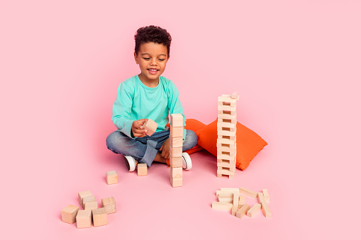 Full body photo of cute little boy play wooden blocks cubes game dressed stylish cyan clothes isolated on pink color background.
