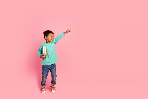 Full body photo of cute little boy hold books flying superhero dressed stylish cyan clothes isolated on pink color background.