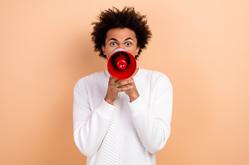 Photo of aggressive man holding bullhorn shouting giving command isolated on beige color background.