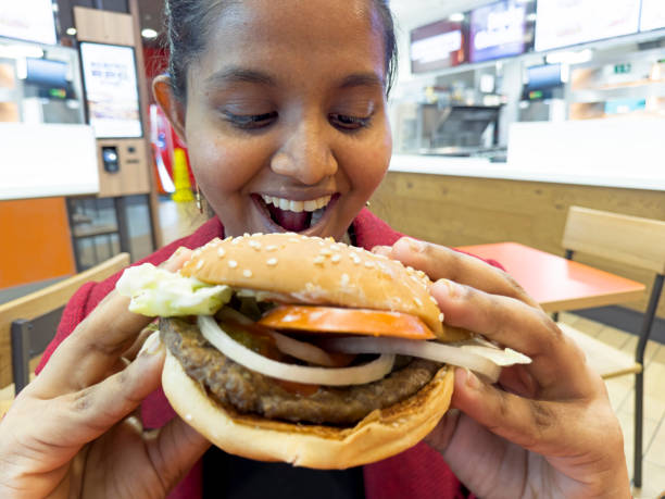 istock Young woman enjoys hamburger at cafe 2149989740