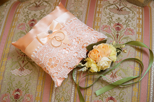Wedding rings made of gold lie on a pink pillow next to a boutonniere of roses