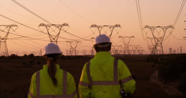 istock Power lines, engineering and people at sunset for electricity, circuit and voltage infrastructure. Construction, teamwork and back of technicians with wires, grid and cable for electrical maintenance 2149993374