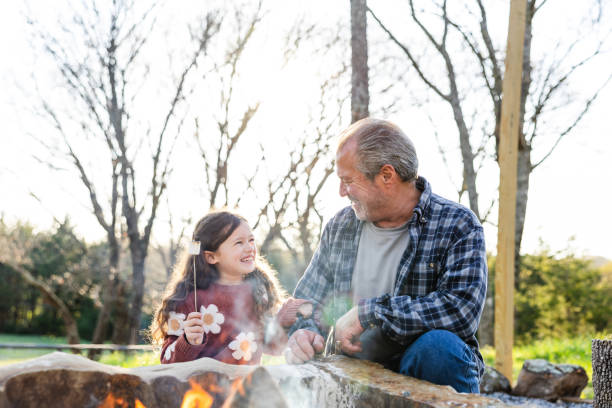 istock Elementary age granddaughter and senior grandfather roast marshmallows 2149995290