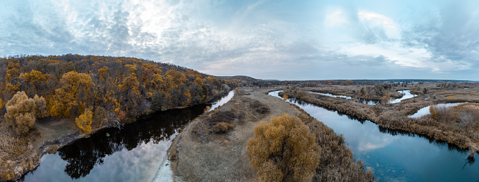 Aerial autumn river valley panorama with trees on riverside and blue cloudy sky in Ukraine