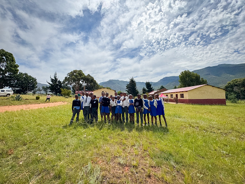 Wide shot Group of African school children in uniform standing on grass in front of a rural school in Malealea, Lesotho.