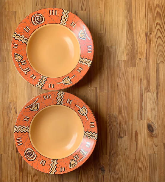 istock Two large round deep empty orange plate with ethnic ornament on a wooden background on the side. View from above. 2149996921