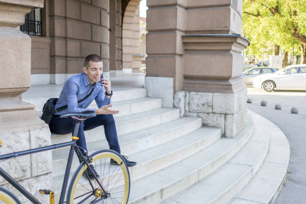 istock Smiling businessman commuter using mobile phone. He is sitting on stairs, taking a rest during his bicycle trip from work after a long workday. 2149997362