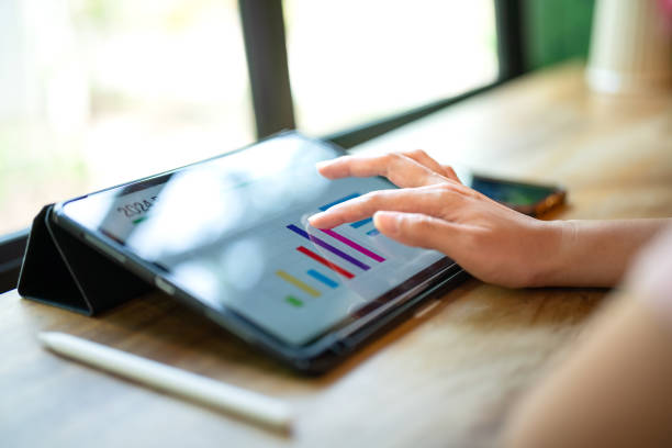 Action of a person hand is touching on tablet screen to review the 2024 business investment plan with graph and chart data. Business working with technology concept, close-up and selective focus.