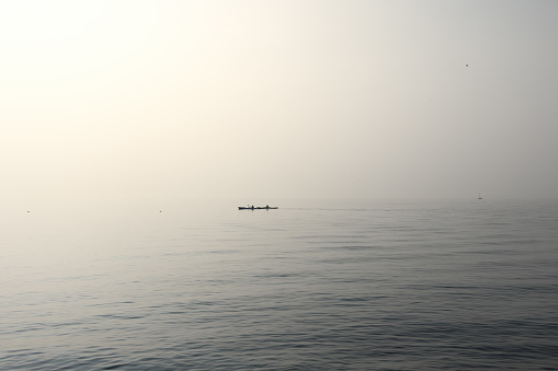 A serene vista captures two canoes gliding over Lake Garda placid waters, enveloped in the soft embrace of morning fog, accentuating the tranquil atmosphere