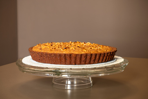 This inviting nut strewn pie, displayed on an elegant glass cake stand, features a perfectly baked, golden crust that tempts with homemade goodness