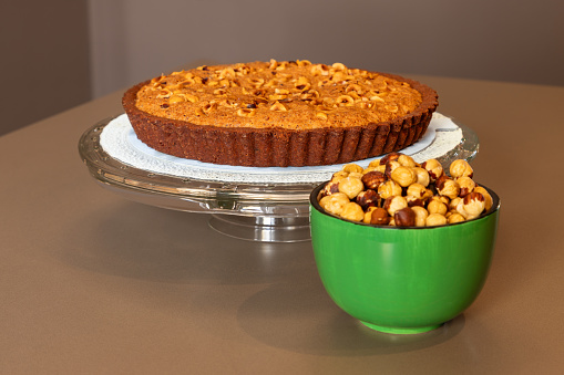 The traditional Italian dessert, a homemade chocolate tart topped with hazelnut cream, is showcased with a vibrant green bowl of roasted hazelnuts