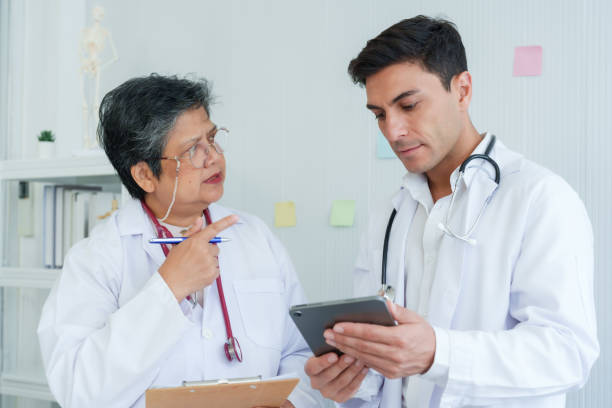 istock Teaching Senior doctor with clipboard exchanges views with attentive resident doctor on tablet use, white clinic office setting underscores learning. Senior medical tutor discusses case with intern focusing 2149999447