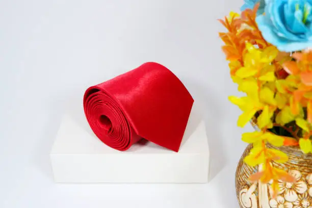 Plain fabric red necktie rolled on white gift box with flowervase together close up view