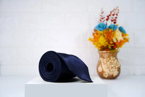Single plain black color necktie rolled on white gift box with background close-up view flowervase together
