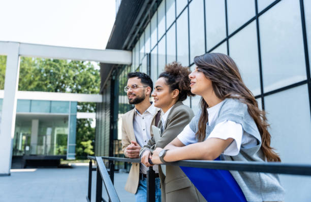 istock Three young business people talking to each other while standing outdoors of office building with suitcase, laptop and register. Group of professional workers discussing about job and plans outside 2150002348