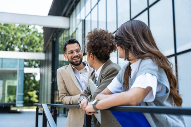 istock Three young business people talking to each other while standing outdoors of office building with suitcase, laptop and register. Group of professional workers discussing about job and plans outside 2150002351