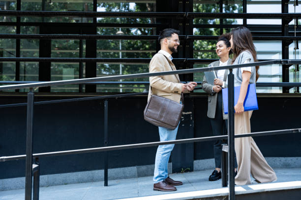 istock Three young business people talking to each other while standing outdoors of office building with suitcase, laptop and register. Group of professional workers discussing about job and plans outside 2150002360