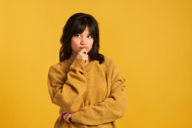 istock A woman in a yellow sweater is looking down and thinking 2150002569