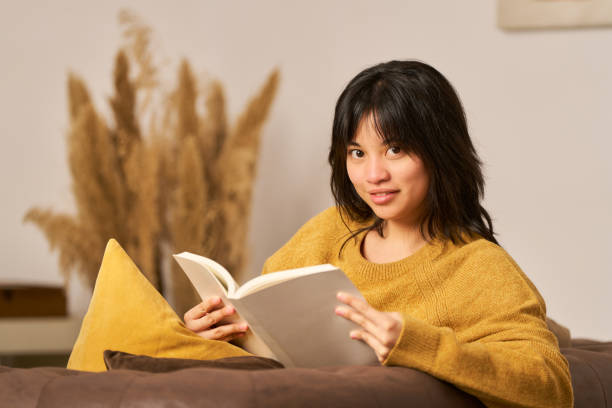 istock A woman is sitting on a couch reading a book 2150002595