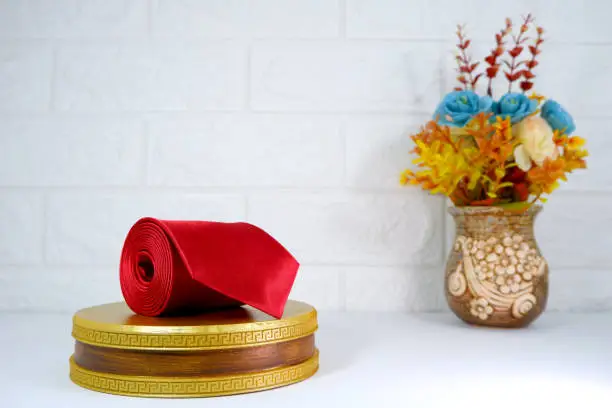 Plain fabric red necktie rolled on display board with flowervase together closeup view