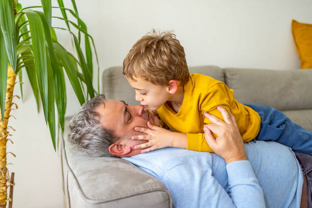 istock Caucasian boy kissing his father, while both lying and relaxing on the sofa 2150003257