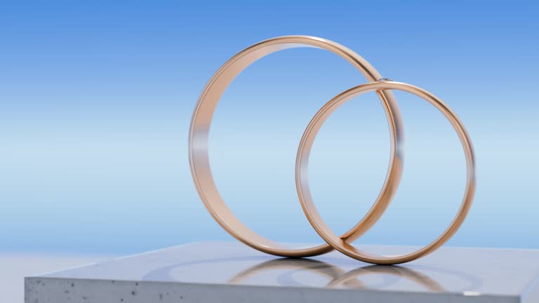 Two gold wedding rings stand on a concrete podium against the sky. The camera rotates around two gold wedding rings.