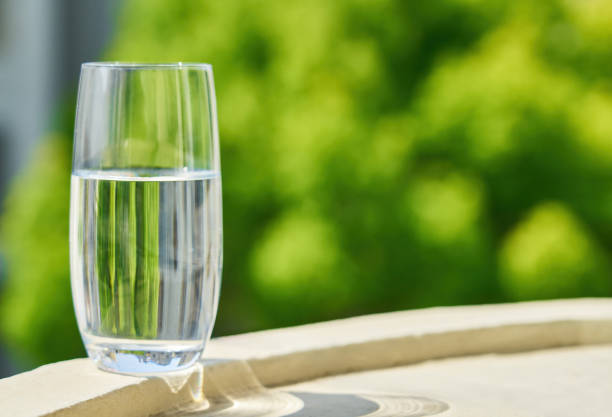 Drink water in glass over sunlight and natural green background.Select focus blurred background.Water for clean health.