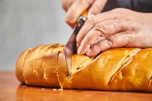 Close-up image of young woman cutting fresh French baguette on wooden board at kitchen counter