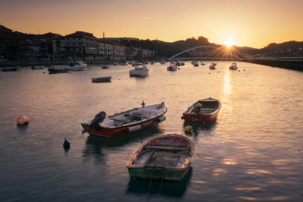 Boats at dawn in the Plentzia estuary with the sun rising behind the mountains leaving a warm atmosphere and an orange sky