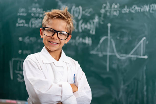 Little scientist solving advanced mathematical problems. The boy is wearing a lab coat and smiling at the camera.\nShot with Nikon D850