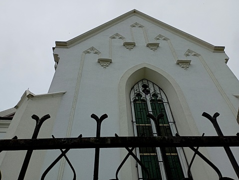 The facade of the ancient church. Buildings and architecture. Metal wrought iron fence and wall with narrow tall vintage window.