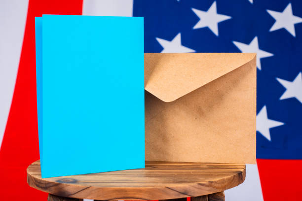 istock Envelope for postal voting. Absentee voting on US voices. Blue billboard next to envelope. US flag in background. Concept - presidential election in united states. Letter from ballot for election 2150015638