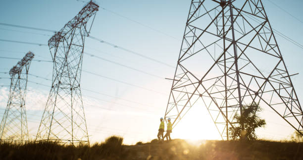 People, engineers and transmission tower for electricity lines or industrial engineering, voltage or infrastructure. Sunset, pylon and pole or cables with blue sky for circuit, current or connection