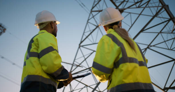 istock People, electrical engineer and tablet in power station with inspection for electricity transmission or tower check. Engineering, collaboration and data transfer for energy distribution and low angle 2150017403