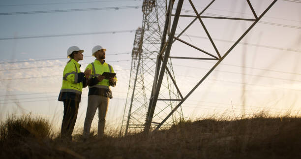 istock People, engineering and transmission tower with tablet for electricity teamwork or safety inspection, pylon or cables. Industrial, wires and power voltage or grid with lines, metal or infrastructure 2150017406