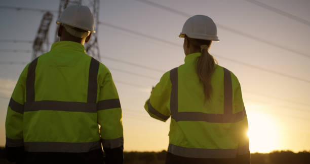 istock Teamwork, electrical engineer and construction in power plant with sunset for electricity inspection and tower check. Engineering, rear view and collaboration for energy distribution and maintenance 2150017407