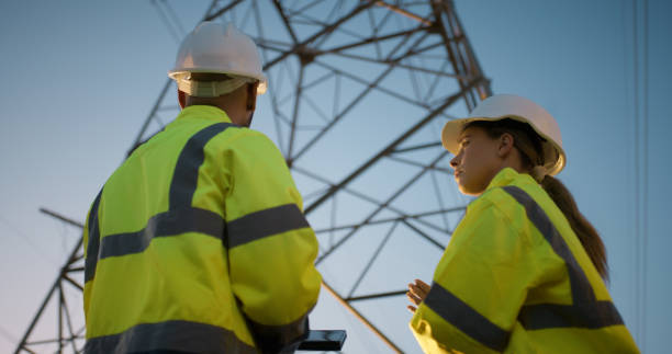 istock Teamwork, electrical engineer and tablet in power station with sunset for electricity transmission and tower check. Engineering, rear view or collaboration for energy distribution and data transfer 2150017411