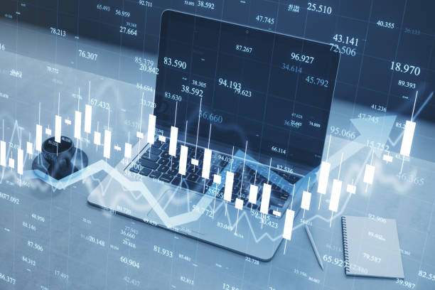 istock Close up of toned workplace with laptop, coffee cup and creative blue candlestick forex chart and growing arrow on blurry background. Trade, finance and stock concept. Double exposure. 2150017716