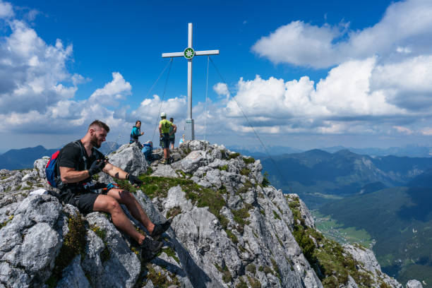 Salzburg, Austria - June 24, 2020: People resting and taking photos next to the cross a top of Mountain Grosser Donnerkogel