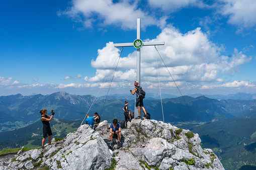 Salzburg, Austria - June 24, 2020: People resting and taking photos next to the cross a top of Mountain Grosser Donnerkogel