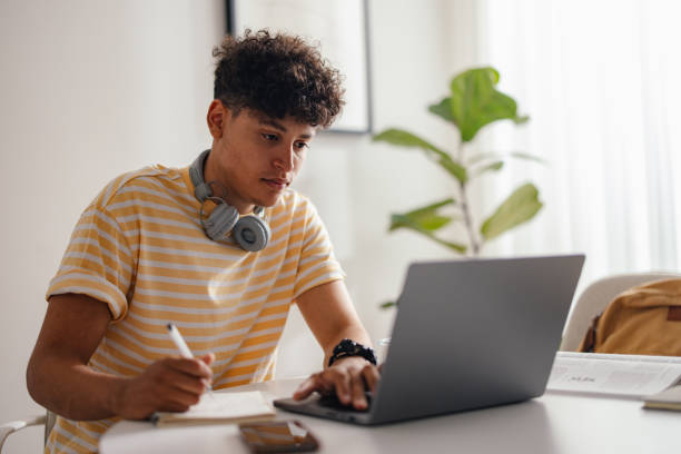 Young Man Studying at Home with Headphones and Laptop