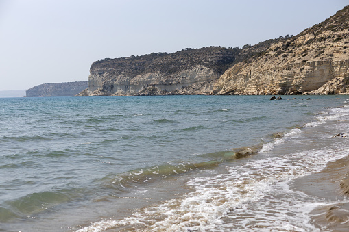 A sandy beach with gentle waves on the Cyprus coast, showcasing cliffs.